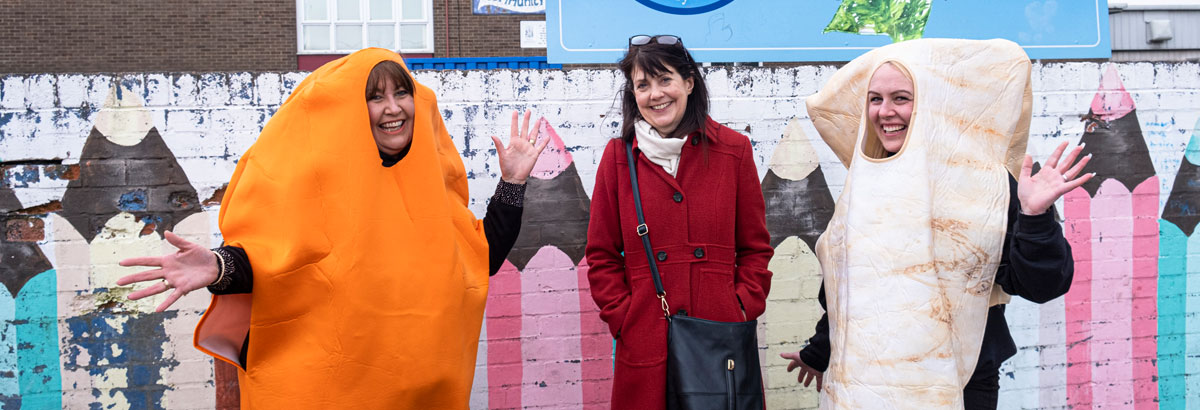 Three people standing in a playground - one is dressed as a carrot, one is dressed as a parsnip