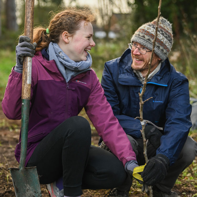 Two smiling people planting a tree with a shovel