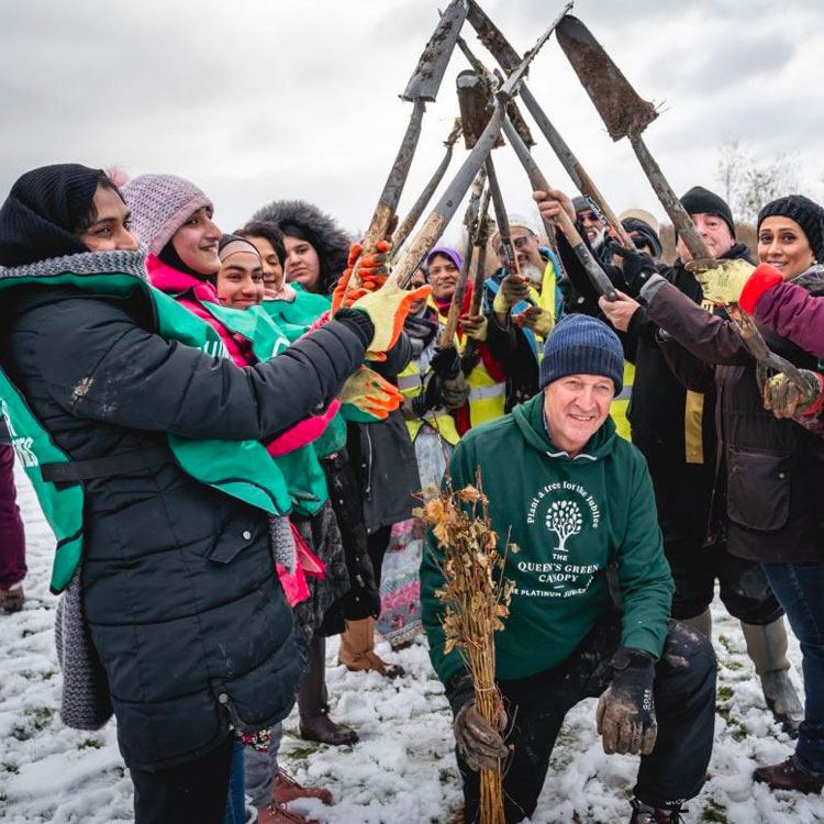 A group of people have made an arch of raised shovels. Another person is kneeling underneath holding dried flowers